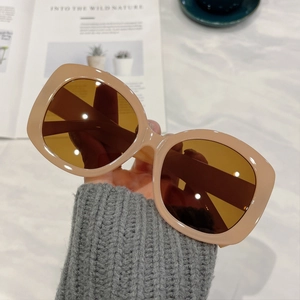 Chic beige square oversized sunglasses with brown lenses held by hand against a marble desk