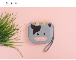 Detail view of a cute blue cow cartoon wallet with hand strap on a soft pink background
