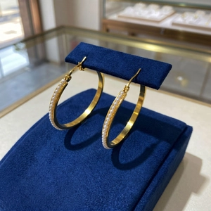 Close-up of 40mm gold hoops with micro-set pearls on a dark blue velvet display stand