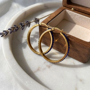 Detailed macro view of 18k gold hoop earrings with blue rhinestones on stone tray