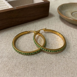 Detail of 40mm gold stainless steel hoop earrings with inlaid green crystals