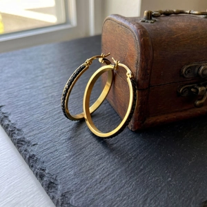 Close-up of 40mm gold stainless steel hoop earrings with black crystal inlay on slate