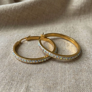 Detail view of 18k gold plated 40mm hoop earrings with AB rhinestones on linen background