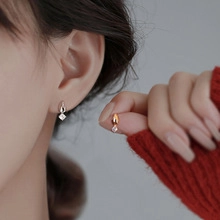 Close-up of minimalist drop stud earrings with square zircon pendant in silver and gold