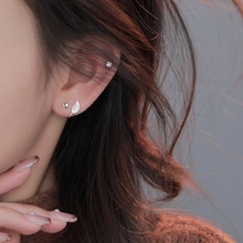 Close-up of minimalist leaf-shaped stud and small silver earrings worn on ear