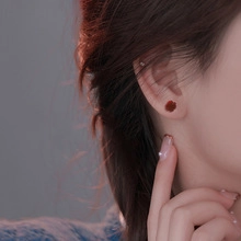 Close-up of a minimalist red petal stud earring on a model with a soft bokeh background