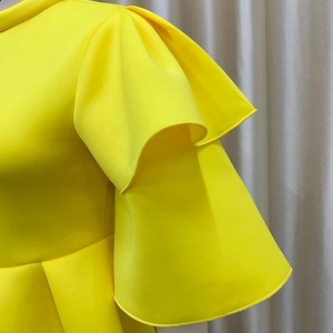 Detail of elegant bright yellow dress featuring layered ruffle sleeves and fine stitching