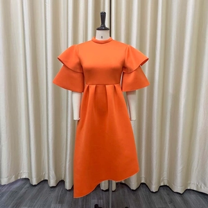 Detail of orange high neck dress featuring structured layered ruffle sleeves and asymmetrical hem