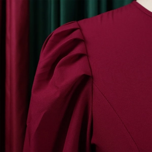 Dettaglio dei drappeggi sulle spalle e maniche a sbuffo bordeaux dell'abito elegante