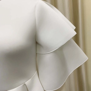 Detail of white dress featuring double-layered ruffled sleeves and premium matte fabric