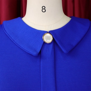 Detail of royal blue dress neckline featuring a pearl button with gold trim