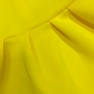Detail of a bright yellow maxi dress showing a wide pleated skirt and precise stitching