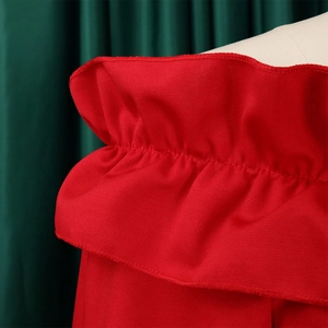 Détail d'une robe rouge à épaules dénudées avec volants sur fond plissé vert foncé