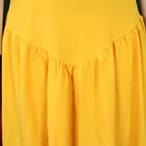 Dettaglio dell'abito giallo brillante con eleganti cuciture a V e vita plissettata