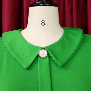 Close-up of Peter Pan collar on green textured dress with a pearl button detail