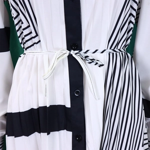 Dettaglio del tessuto plissettato del vestito a righe bianche e nere con bottoni e cintura