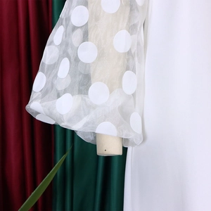 Detail eines weißen Kleides mit eleganten Mesh-Puffärmeln und großem Punktemuster