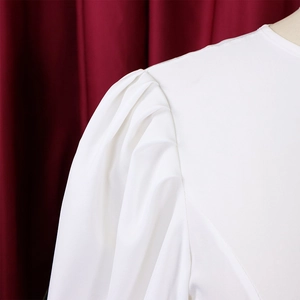 Dettaglio di un abito bianco che mostra eleganti maniche a sbuffo con pieghe sulle spalle