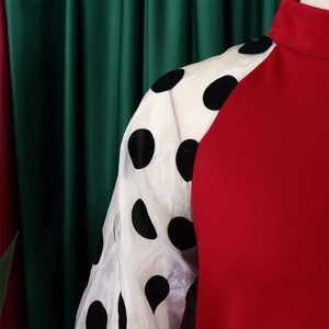 Detail eines roten Stehkragenkleids mit weißen Netzarrmeln und großen schwarzen Punkten