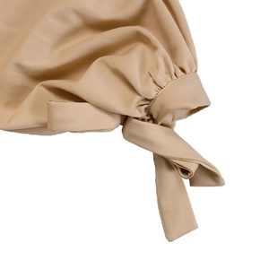 Detailed close-up of beige knit dress featuring elegant waist bow tie and pleated fabric