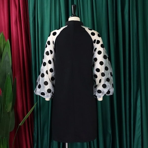 Detail eines schwarzen Kleides mit weißen Polka-Dot-Netzärmeln und einem Stehkragen
