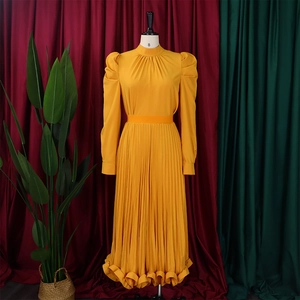 Close-up of golden pleated dress showing the high neck detail and textured fabric