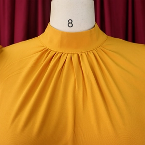 Detail of mustard yellow high neck pleated top with refined fabric texture and stitching