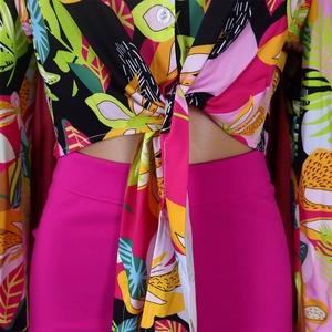 Detail of tropical print shirt with front tie knot and fuchsia high waist trousers