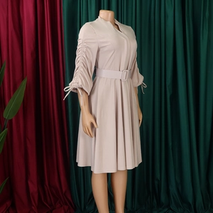 Détail d'une robe trapèze beige avec col en V, manches plissées à cordon et ceinture assortie