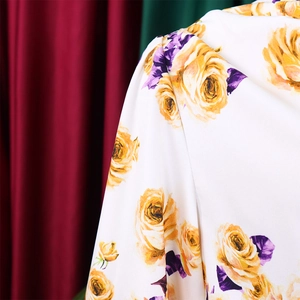 Détail du tissu à fleurs avec roses jaunes et feuilles violettes sur fond blanc