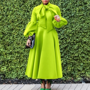 Lime green long dress with lantern sleeves and a bow neckline against a green wall