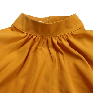 Detailed view of mustard yellow puff sleeve top featuring pleated high collar neckline