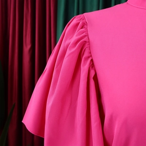 Detail of rose red dress showing flare sleeve texture and elegant pleated shoulder seams