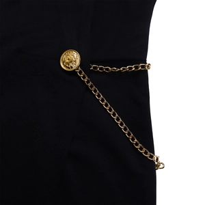 Detail of elegant black fabric featuring a gold lion embossed button and metal chain link