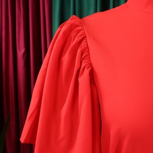 Detail of red flare sleeve dress showing pleated shoulder design and smooth fabric texture