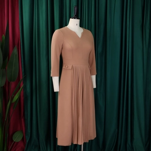 Detail of the camel V-neck dress featuring unique side pleats and elegant decorative pockets