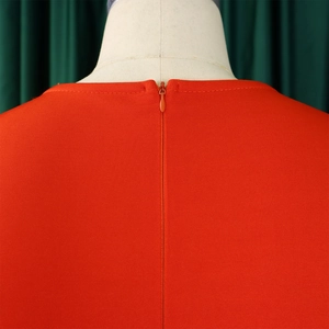 Detail of an orange-red pleated evening dress featuring a seamless invisible back zipper