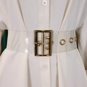 Detailed shot of transparent PVC belt with gold metal buckle on a white dress