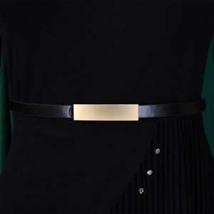 Détail d'une boucle en métal doré sur une fine ceinture noire minimaliste et élégante