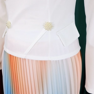 Detailed view of white slim jacket with pearl embellishment and gradient pleated skirt