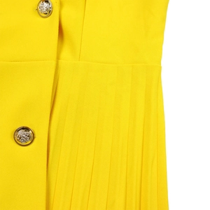 Detail of yellow pleated dress featuring decorative golden lion head metal buttons