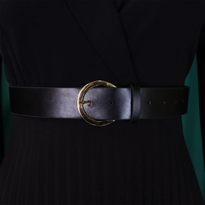 Détail d'une large ceinture en cuir noir avec boucle dorée ronde sur une robe plissée