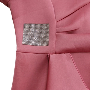 Close-up of pink ruffle dress showing sparkling rhinestone patch detail on smooth fabric