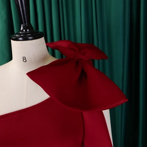 Detail of the large 3D bow on the one-shoulder red evening dress displayed on a mannequin