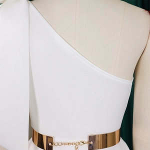 Detail of one-shoulder white dress featuring a metallic gold chain belt decoration