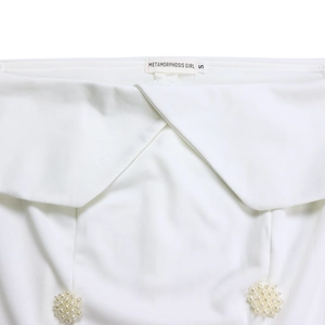 Detail of white off-shoulder top featuring crossed neckline and elegant pearl clusters