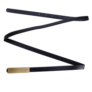 Détail d'une ceinture fine en cuir noir avec une boucle rectangulaire en métal doré mat