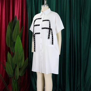 Detail of white shirt dress featuring black tape trim and silver metal eyelet accents