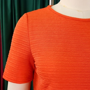 Détail du haut orange à manches courtes montrant le tissu plissé et le col ras du cou