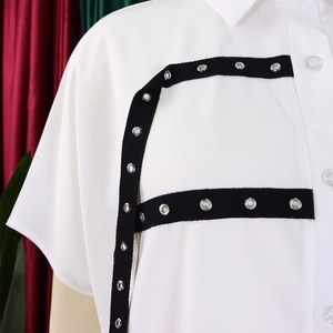 Detail of white cotton shirt featuring black ribbon with silver metal eyelets and white buttons